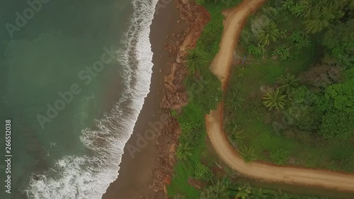 Aerial view of car driving on interesting dirt road between ocean waves and central american jungle moves bottom scene to top photo