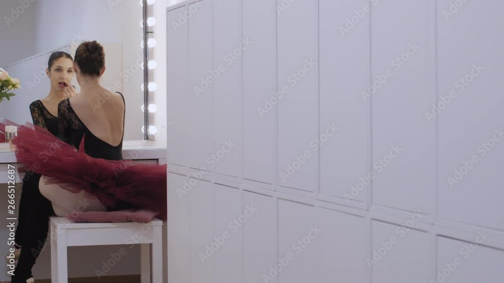 Caucasian ballerina puts on red lipstick in a white dressing room, wide to medium shot Caucasian ballerina puts on red lipstick in a white dressing room, wide to medium shot