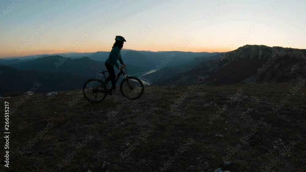 Girl riding a bike uphill on a mountain at sunset. Beautiful canyon lake in the background.