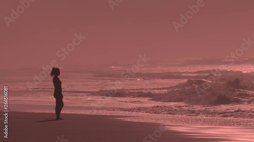 Woman takes in the beautiful sunset in Hawaii. The waves crash in slow motion and the sun sets with an orange light diffused by the oceans mist. photo