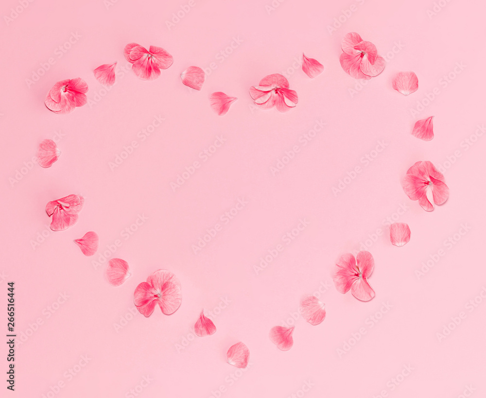 Flat lay composition of pink flowers in a shape of heart on pastel pink background.