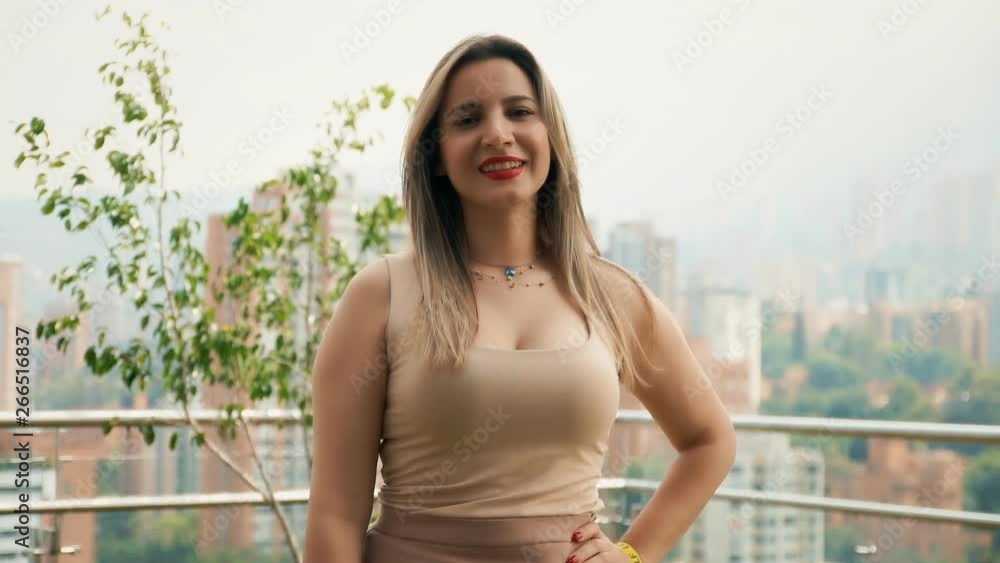 A pretty woman, looking at the camera and smiling while standing on the rooftop of a high building (big city skyline). Handheld shot. A pretty woman, looking at the camera and smiling while standing on the rooftop of a high building (big city skyline). Handheld shot.