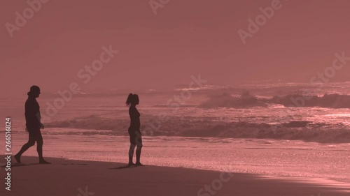 Male joins Female to enjoy sunset in Kauai, Hawaii. Big waves crash in slow motion as the sky is lit up orange from the sunset and the diffusing ocean mist. photo