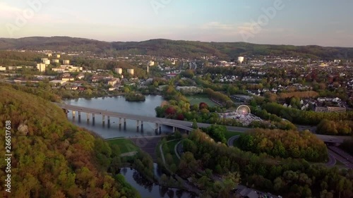 AERIAL, impressive view of a small town surrounded by a wooded area with some hills in the background, and in the foreground a bridge over a lake