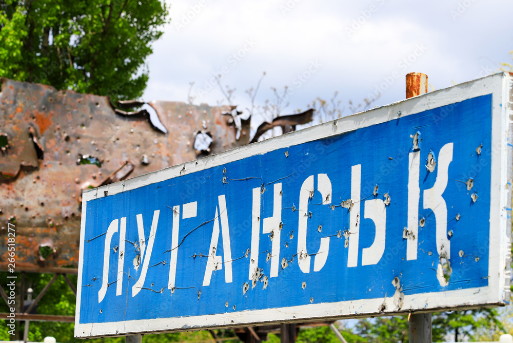 Blue road sign with the inscription in Ukrainian Lugansk, punched by bullets during the war in the Donbass, conflict East Ukraine, Ukrainian war Blue road sign with the inscription in Ukrainian Lugansk, punched by bullets during the war in the Donbass, conflict East Ukraine, Ukrainian war