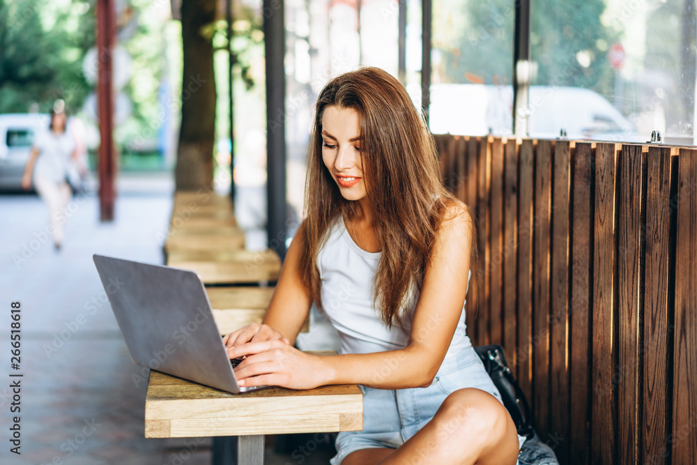 Pretty young girl working on laptop in street cafe outdoor. Pretty young girl working on laptop in street cafe outdoor.