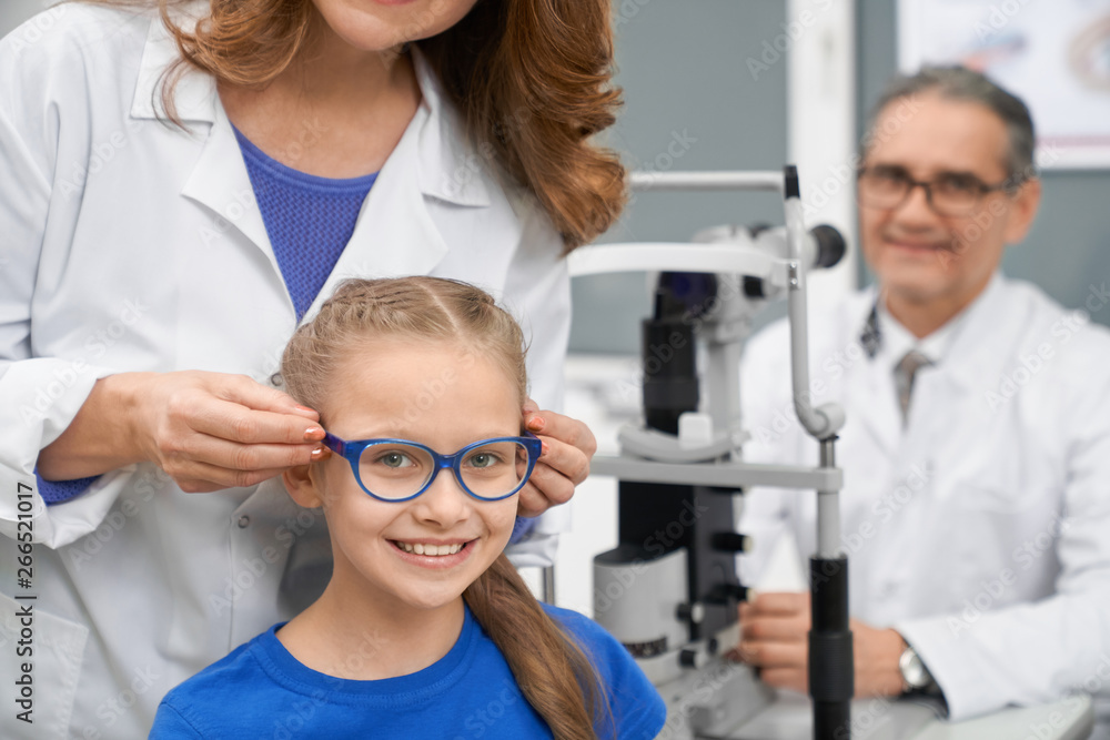 Medical worker choosing glasses for pretty teenage girl. Medical worker choosing glasses for pretty teenage girl.
