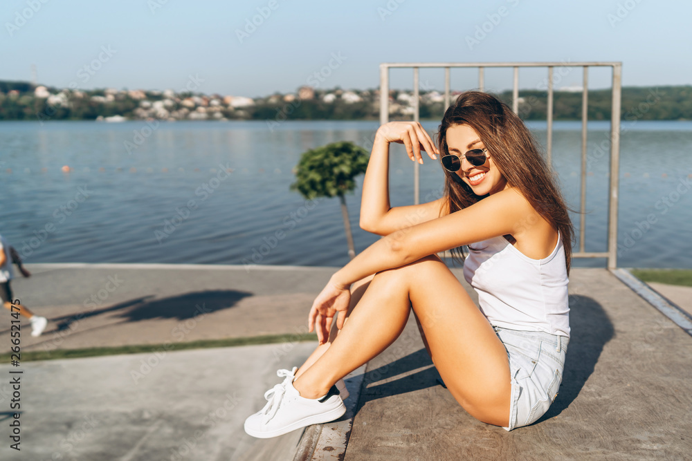 Pretty young brunette girl with long hair relaxing outdoor in the park near lake.