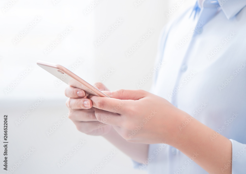 Side view of asia young business woman in blue shirt dress standing beside window and using smart phone in bright office room, copy space, close up Side view of asia young business woman in blue shirt dress standing beside window and using smart phone in bright office room, copy space, close up