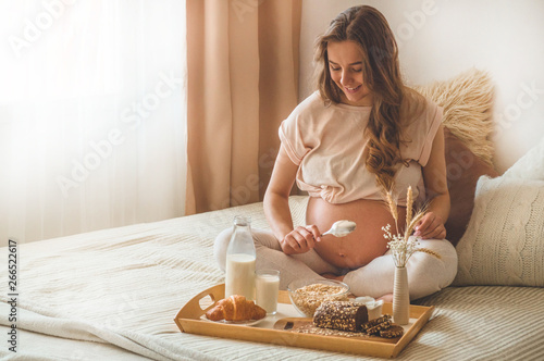 Pregnancy and healthy organic nutrition. Pregnant woman enjoying breakfast with oatmeal in bed, free space. Concept of expectation and health.