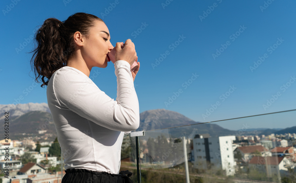 Young woman drinking coffee or tea on balcony with beautiful landscape panorama