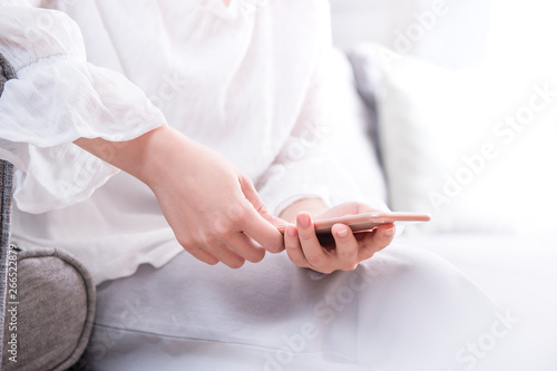 Side view of asia young woman in white sitting on sofa and using smart phone in bright living room  copy space  close up  blank for design concept