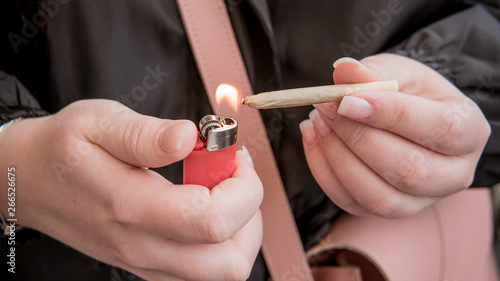 Marijuana joint in the female hand close-up. Woman smoking medical marijuana joint uotdoors.