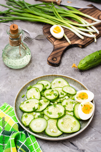 Fresh cucumber salad, boiled chicken eggs and green onions on a plate and ingredients for cooking on the table