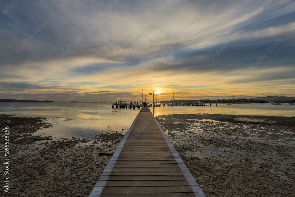 Timber jetty leading to sun setting over ocean at low tide