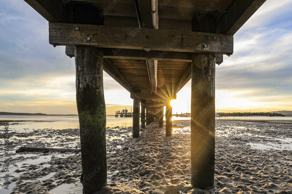 Timber jetty leading to sun setting over ocean at low tide