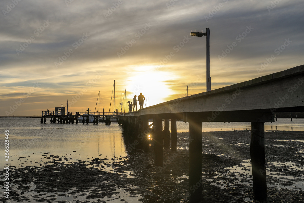 Timber jetty leading to sunset with silhouettes