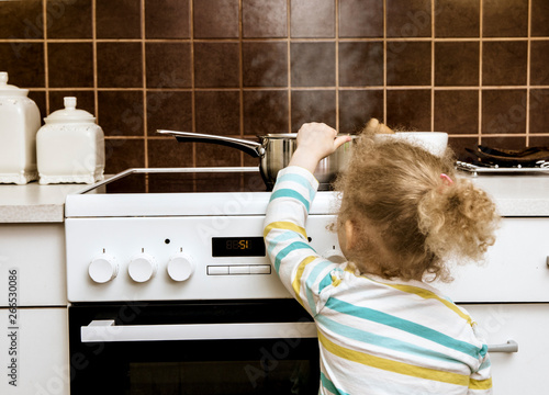 Accident waiting to happen. Toddler girl pulling boiling pot of water over in home kitchen. Hazard at home, skin burn concept( set up, pot is empty).
