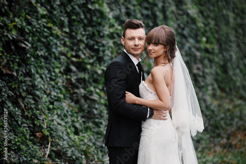 Stylish couple of newlyweds on their wedding day. Happy young bride, elegant groom and wedding bouquet. Portrait of young wedding couple at nature. © Andriy Medvediuk