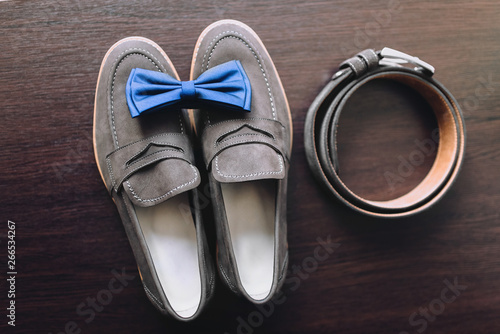 Morning groom and wedding details. Leather gray shoes, a belt and a blue bow tie lie on a background of brown floor close-up. Composition and concept.