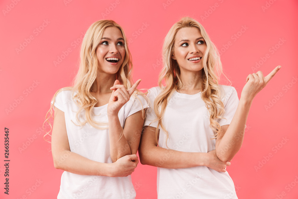 Smiling blonde twins wearing in t-shirts pointing and looking away Smiling blonde twins wearing in t-shirts pointing and looking away
