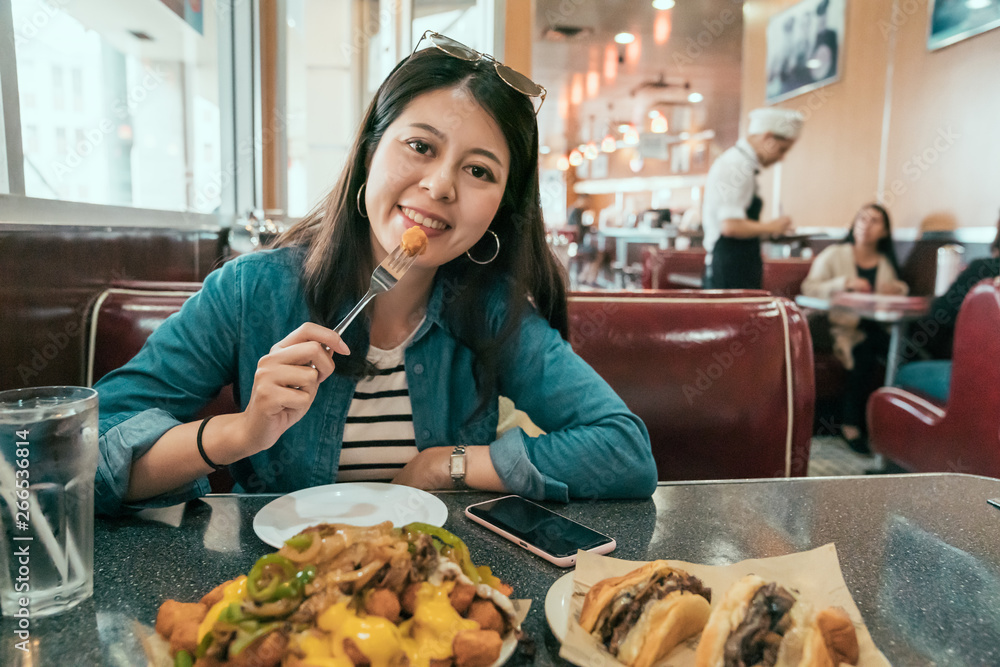asian local woman lifestyle in usa eating fast food and drinking beverage in American diner restaurant. young lady tourist use fork having lunch face camera smiling attractive. waiter customer order