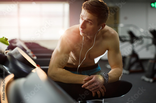Fototapeta Naklejka Na Ścianę i Meble -  Man running in a modern gym on a treadmill concept for exercising, fitness and healthy lifestyle and listening music