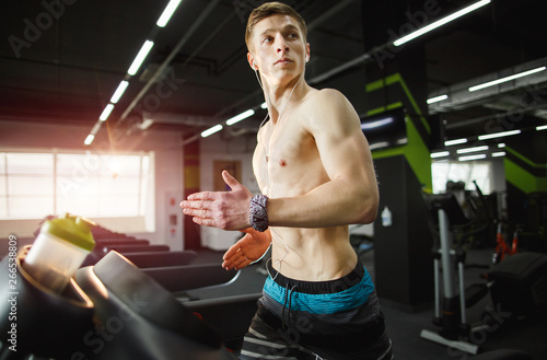 Man running in a modern gym on a treadmill concept for exercising, fitness and healthy lifestyle and listening music