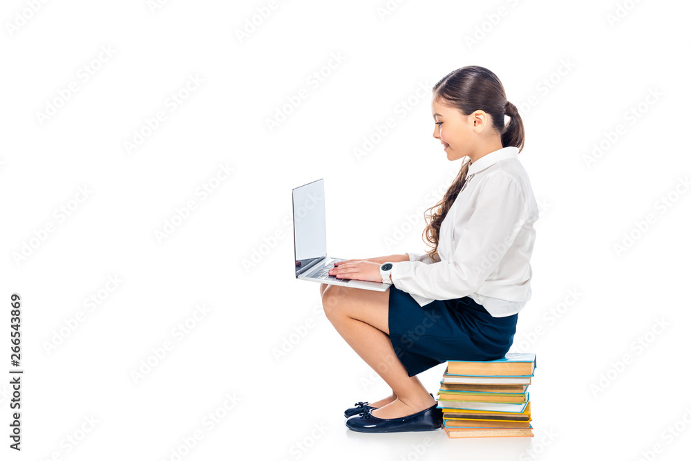 schoolgirl in formal wear sitting on books and using laptop Isolated On White with copy space schoolgirl in formal wear sitting on books and using laptop Isolated On White with copy space