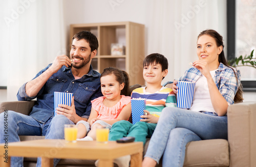 family, leisure and people concept - happy mother, father, son and daughter with popcorn watching tv at home