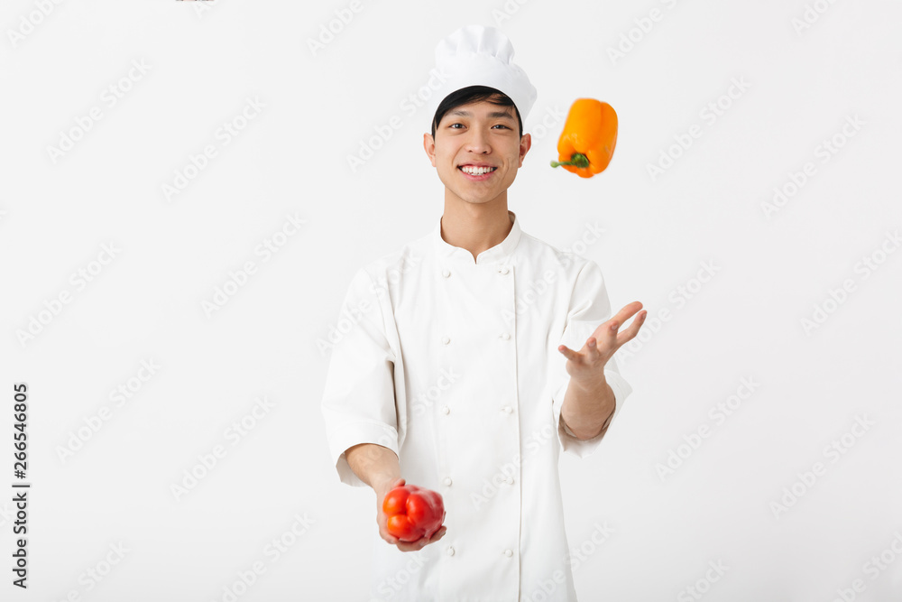 Image of asian professional chief man in white cook uniform smiling at camera while holding sweet papers vegetables Image of asian professional chief man in white cook uniform smiling at camera while holding sweet papers vegetables