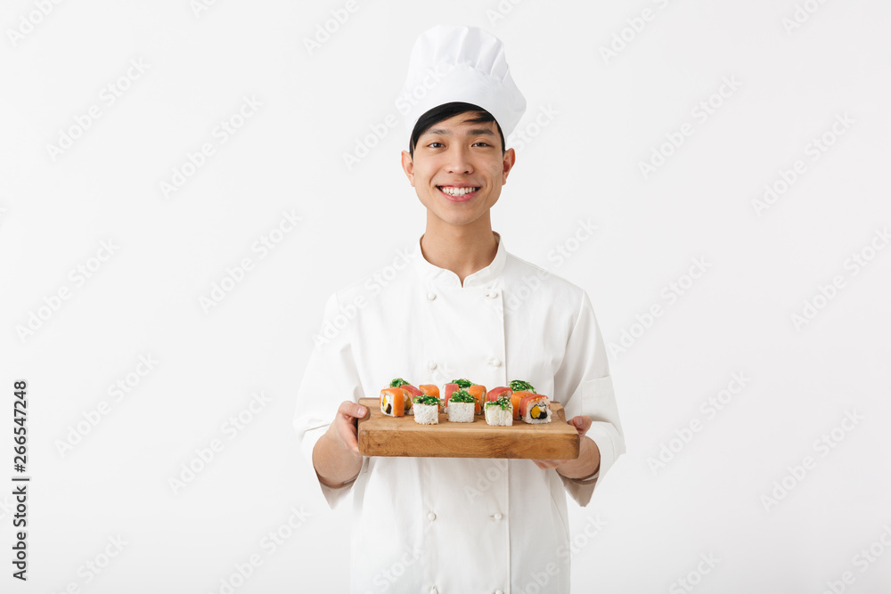 Image of positive chinese chief man in white cook uniform smiling at camera while holding plate with sushi set Image of positive chinese chief man in white cook uniform smiling at camera while holding plate with sushi set