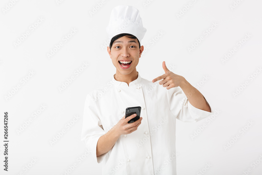 Image of young chinese chief man in white cook uniform and chef's hat holding mobile phone Image of young chinese chief man in white cook uniform and chef's hat holding mobile phone