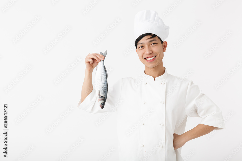 Image of pleased japanese chief man in white cook uniform and hat smiling while holding raw fresh fish Image of pleased japanese chief man in white cook uniform and hat smiling while holding raw fresh fish