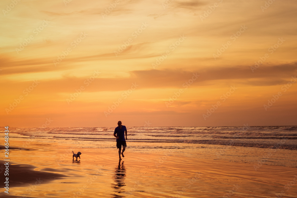 Silhouette of man running with dog in the beach in sunset time