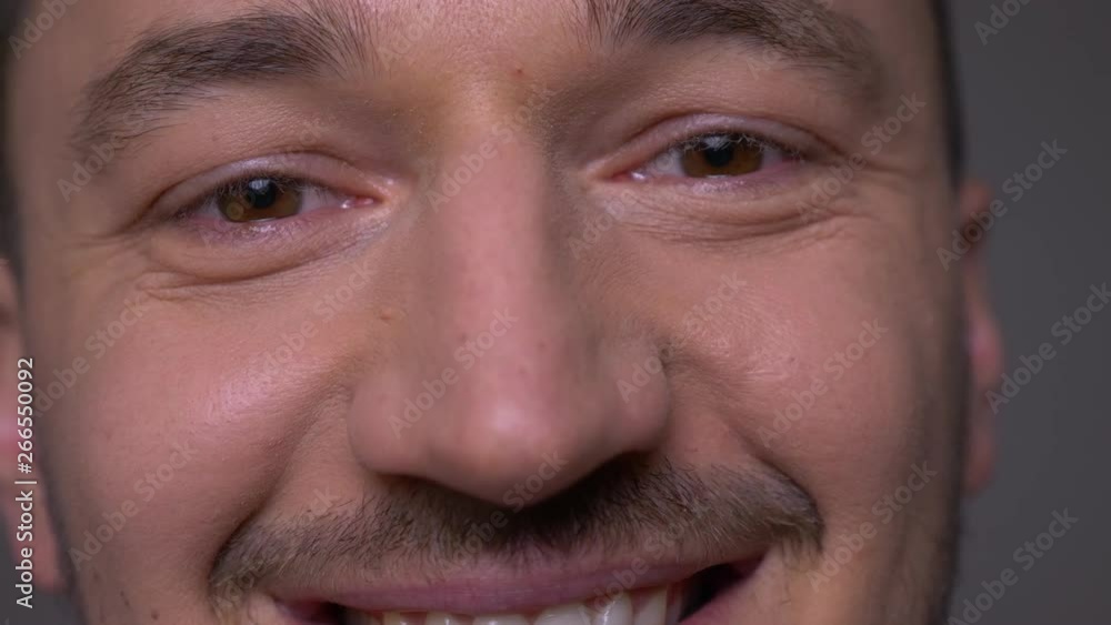 Closeup shoot of young handsome caucasian male face with eyes looking at camera with smiling expression with background isolated on gray Closeup shoot of young handsome caucasian male face with eyes looking at camera with smiling expression with background isolated on gray