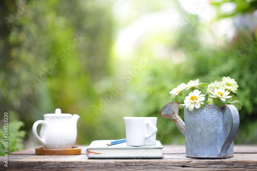 White cup and white pot and flowers in rustic watering pot on wooden table