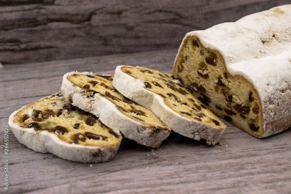 The three slices and the main part of Stollen on a wooden background. Traditional German Christmas cake with marzipan and dried fruits.