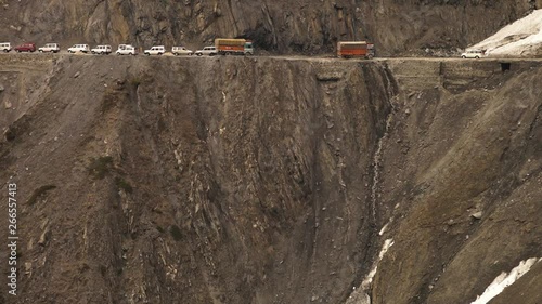 Medium high-angle still shot of off-road vehicles moving downhill, stopping to give way for those travelling uphill. Indian Himalayan glacier has blocked one side of the dangerous mountain pass