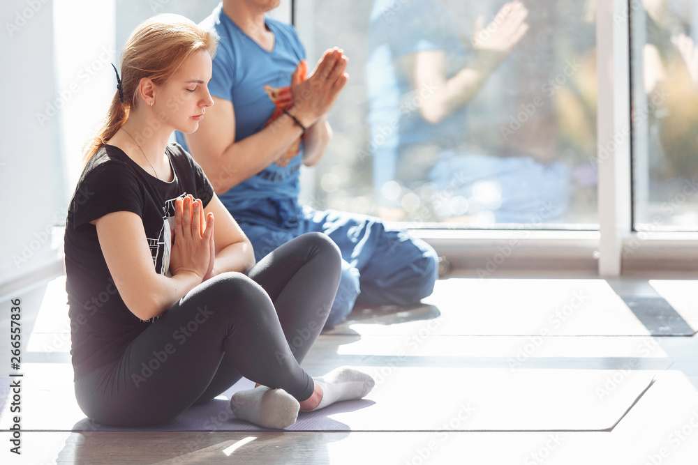Group of young people is meditating while sitting in padmasana in bright gym with large window. Concept of increasing the mobility of the knees and ankles its increased blood circulation in abdomen