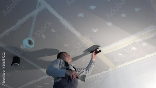 Skilled worker man spackling gypsum drywall ceiling with trowel