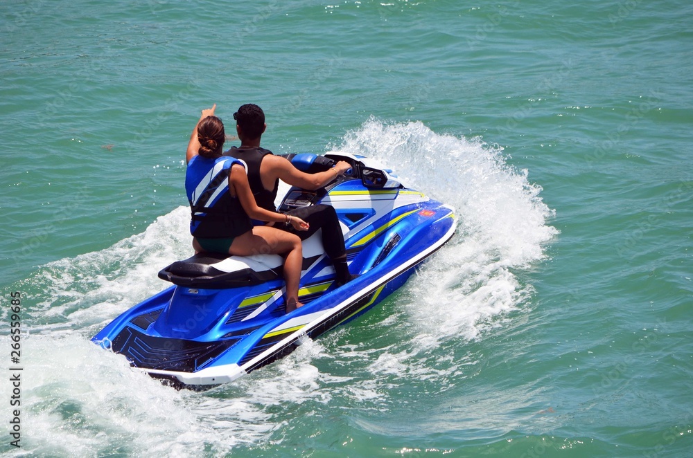 angled elevated view of a young man and a young woman riding tandem on a blue jet ski