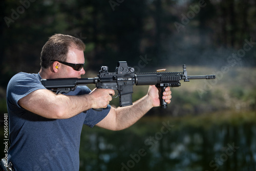 A man shooting an assault rifle with the ejected shell in the air.