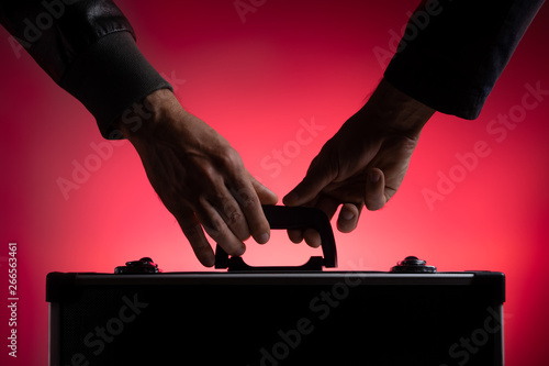 A man passes a metal case to another man. Close-up. Red background. photo