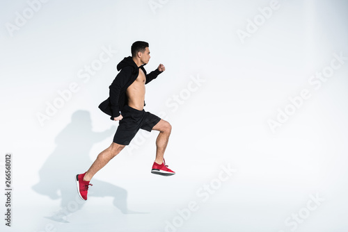 side view of sportive mixed race man in black sportswear running on white