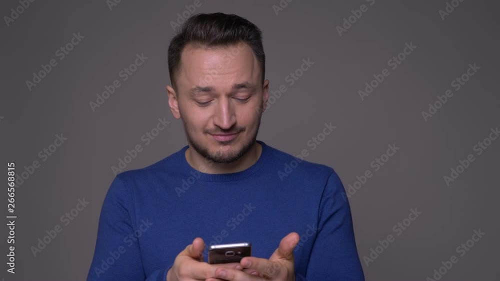 Closeup shoot of young handsome caucasian man messaging on the phone with background isolated on gray Closeup shoot of young handsome caucasian man messaging on the phone with background isolated on gray