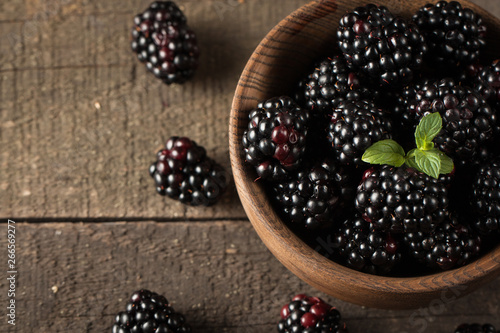 Fresh organic ripe blackberries in a wooden bowl on wooden background. Healthy rustic food concept.