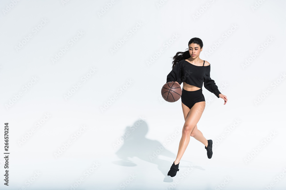 beautiful african american girl in black sportswear and sneakers running and playing ball on white