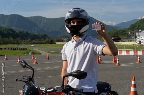 Young man in a helmet on the motorbike is showing driving license