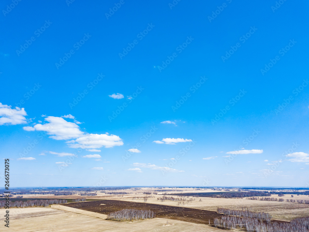 Fototapeta premium Panorama from the air on the lush meadows and fields with colorful plots of agricultural crops before sowing in spring outside the city in the sun under a blue sky and white clouds. Nature in season.